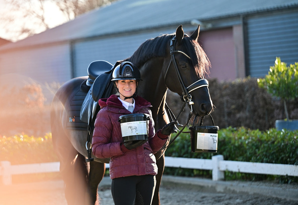 Dinja van Liere staat samen met haar paard. Ze heeft het paardensupplement NerveLess in haar hand van Duval Horse Products. Haar paard heeft het hengsel van de emmer Multipower in zijn mond
